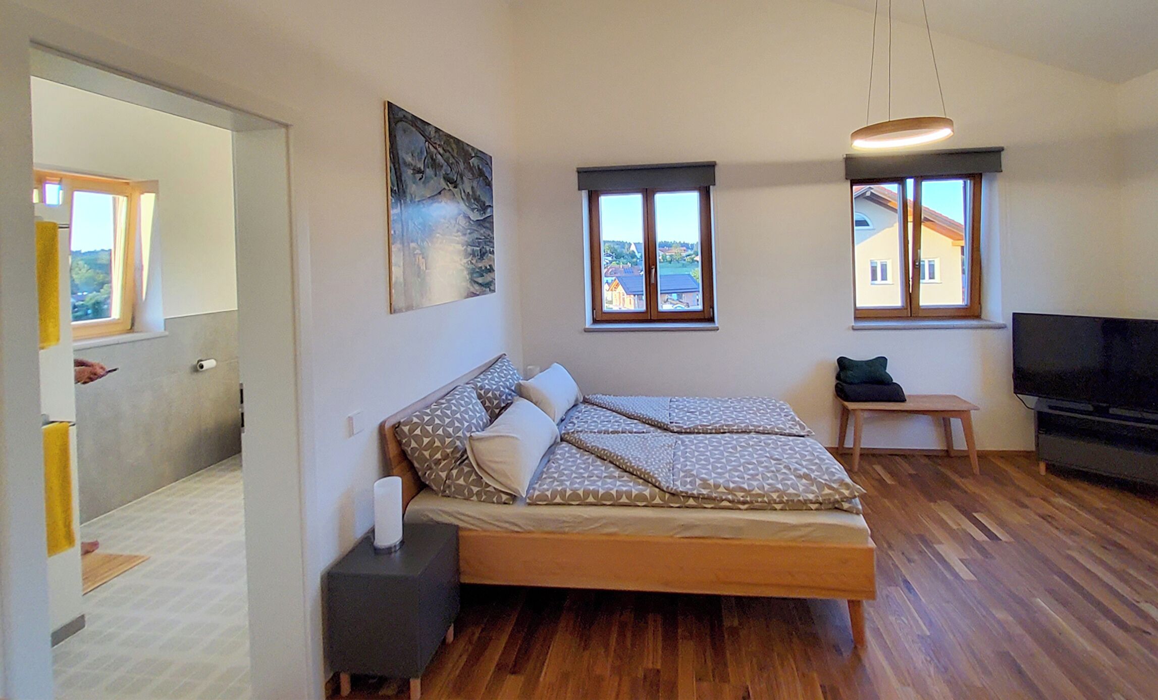Une chambre moderne avec un lit en bois, un téléviseur à écran plat et de grandes fenêtres.