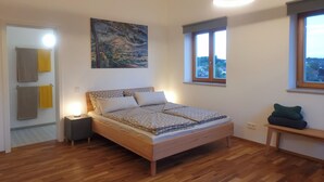 Een slaapkamer met een bed, nachtkastje, raam en een schilderij aan de muur.