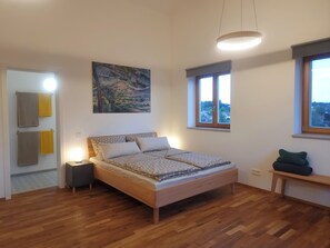 A bedroom with a bed, a nightstand, a bedside table, a window, and a painting on the wall. - Vacation Rental Next to the Ceramics Studio (Babensham)