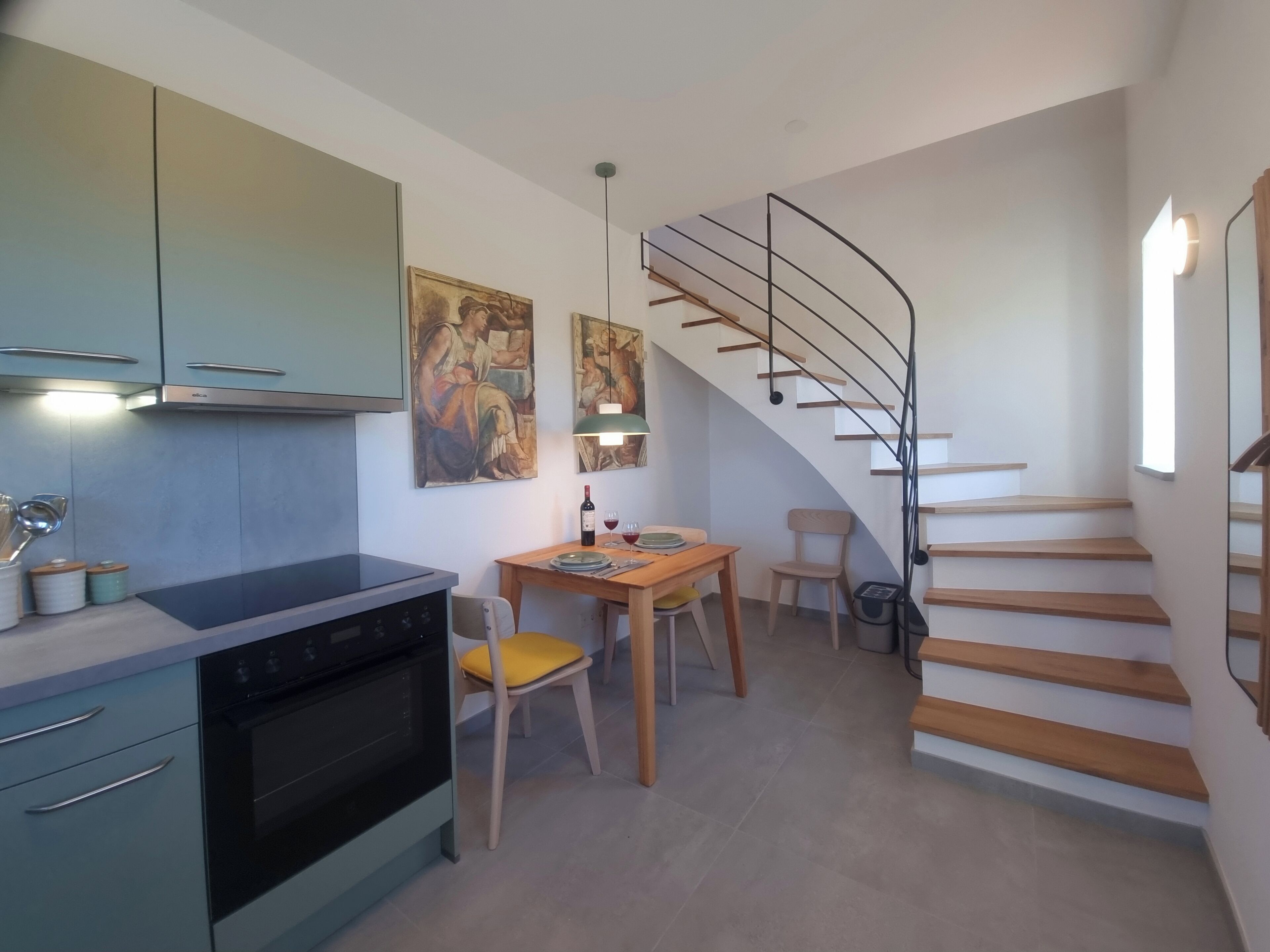 Una cuina moderna amb zona de menjador, una escala i obres d'art a les parets.