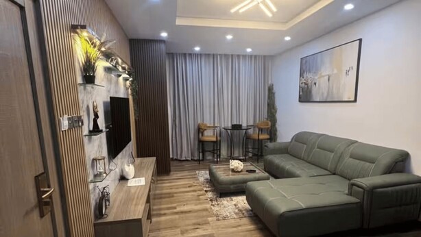 Een moderne woonkamer met een modulaire bank, een houten vloer, een plafondlamp en een eethoek met een tafel en stoelen.