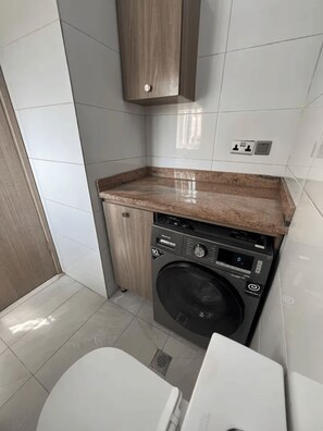 A compact laundry room with a washing machine, a countertop, and a cabinet. - Modern 1-Bedroom Apartment in Lekki 1 with Fast Wi-Fi & 24/7 Power (Lekki)