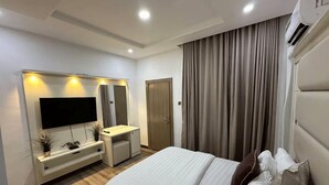 Een moderne hotelkamer met een bed, een televisie, een kaptafel met spiegel en een groot raam met gordijnen.