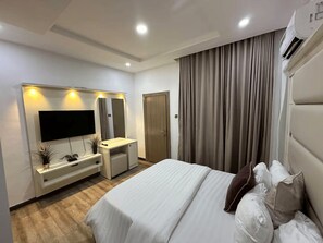 A modern hotel room with a bed, a TV, a vanity with a mirror, and a large window with curtains. - Modern 1-Bedroom Apartment in Lekki 1 with Fast Wi-Fi & 24/7 Power (Lekki)
