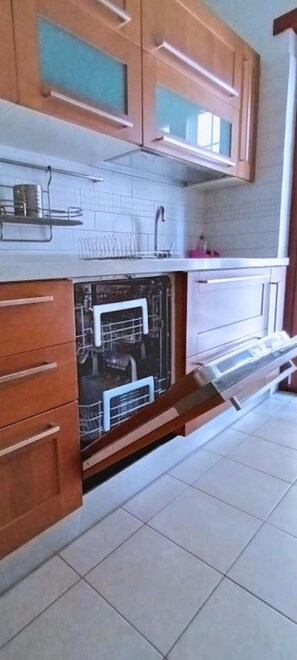 Eine Küche mit Holzausstattung, einem Geschirrspüler und einem gefliesten Boden.