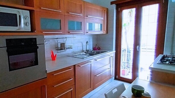 A kitchen with wooden cabinets, a microwave, an oven, a sink, and a window with a view. - Spacious 2-bedroom, 2-bathroom apartment near the Colosseum in Rome (Roma)