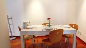 A dining area with a white table set for two, two orange chairs, a vase with a red flower, and a radiator on the wall. - Spacious 2-bedroom, 2-bathroom apartment near the Colosseum in Rome (Roma)