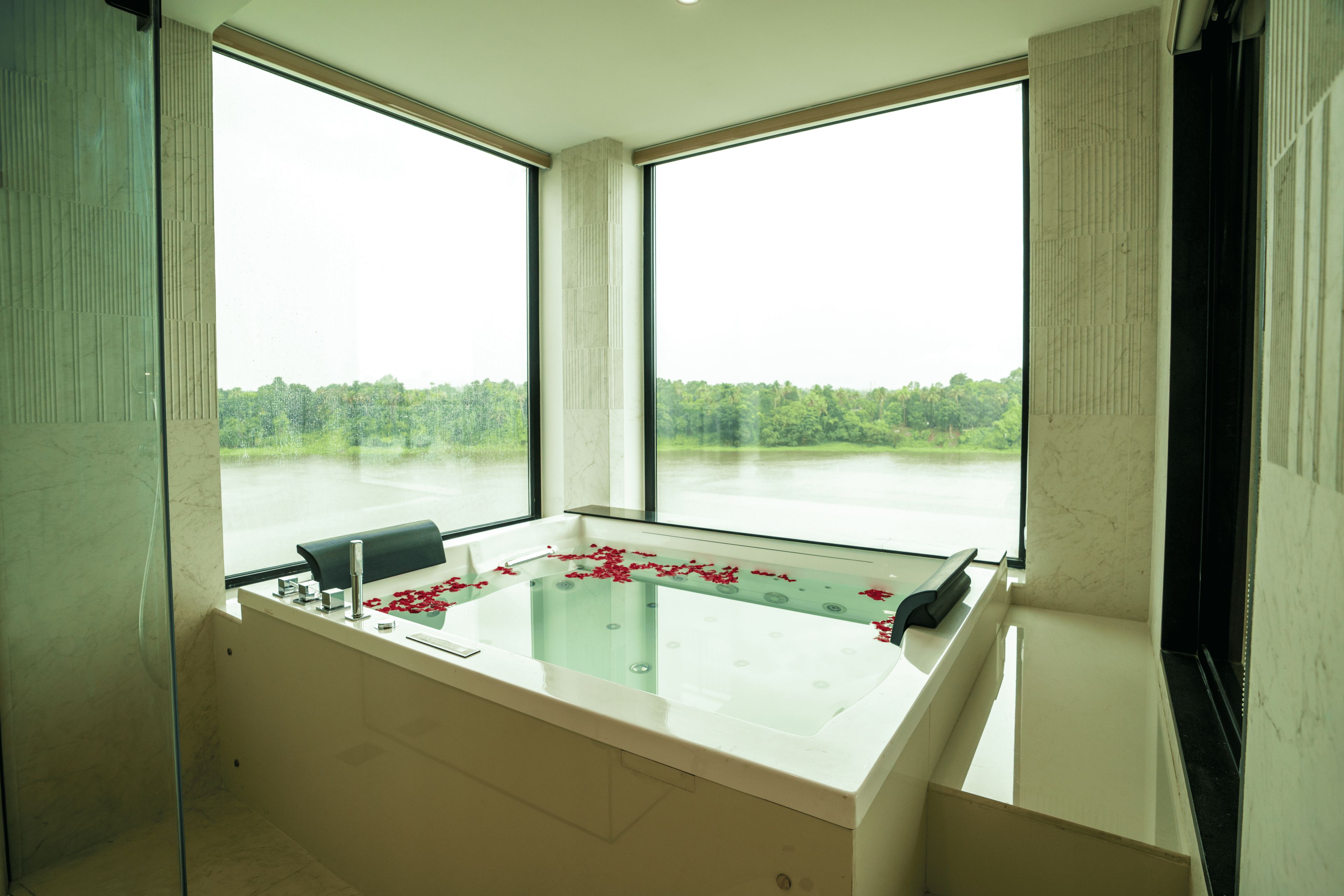 Ein Spa-Raum mit einer Glaskabine für eine Badewanne, Blick auf einen Wald durch große Fenster und einem modernen Design.