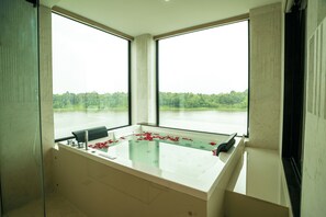 A spa room with a glass-enclosed bathtub, a view of a forest through large windows, and a modern design. - Travancore Palace, Cochin (Aluva)
