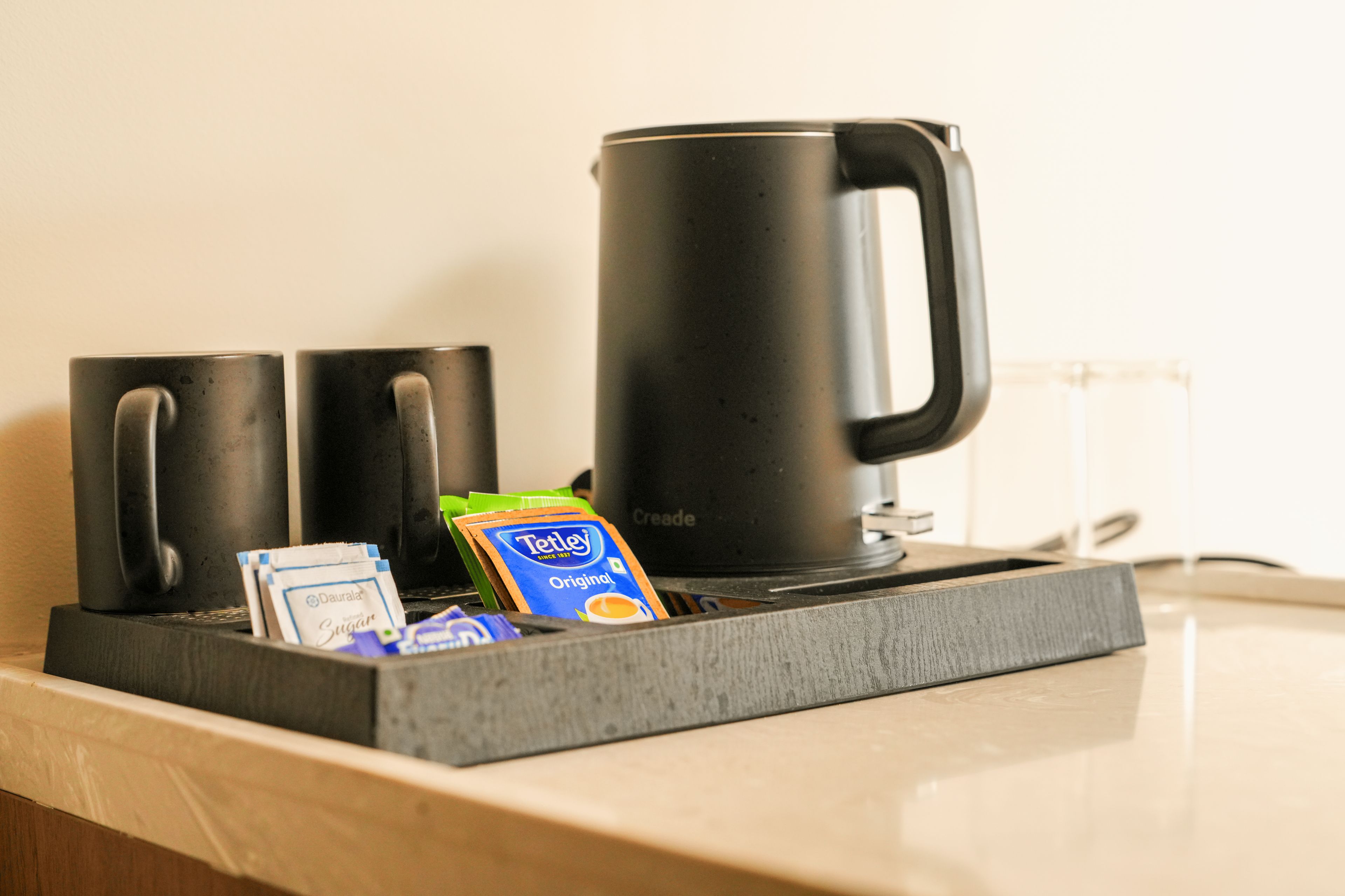 Una macchina da caffè su un piano di lavoro, con un vassoio che contiene una bustina di zucchero, una bustina di panna e una cialda per caffè.