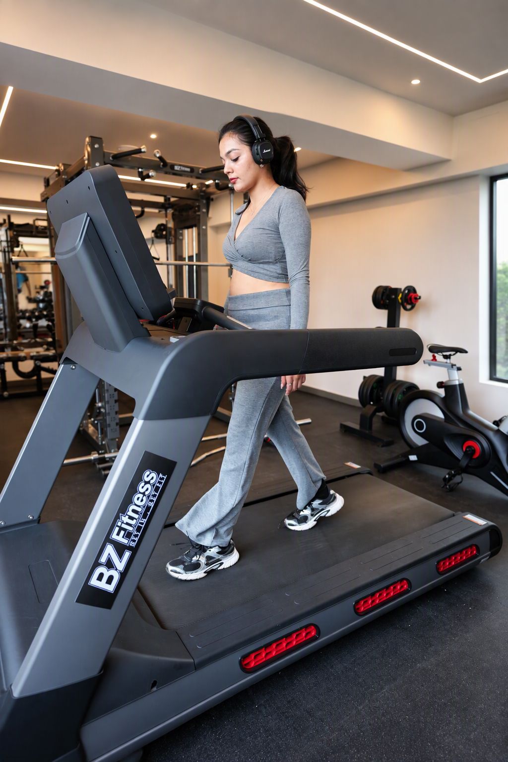 Une femme marche sur un tapis de course dans une salle de sport, avec des appareils d’exercice en arrière-plan.