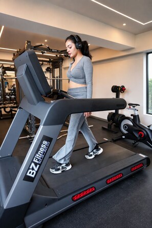 Una mujer camina en una cinta de correr en un gimnasio, con equipo de ejercicio al fondo.