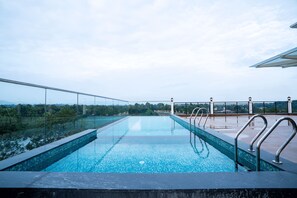 A rooftop infinity pool with clear blue water, surrounded by glass railings and a view of the cityscape. - Travancore Palace, Cochin (Aluva)