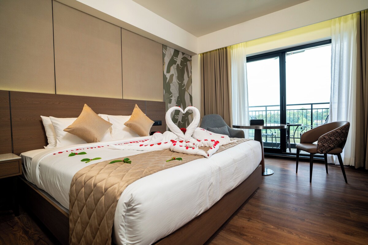 A hotel room with a large bed, a desk, a chair, and a balcony view.