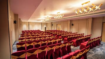 Un salón de conferencias con filas de sillas, un escenario y una puerta.
