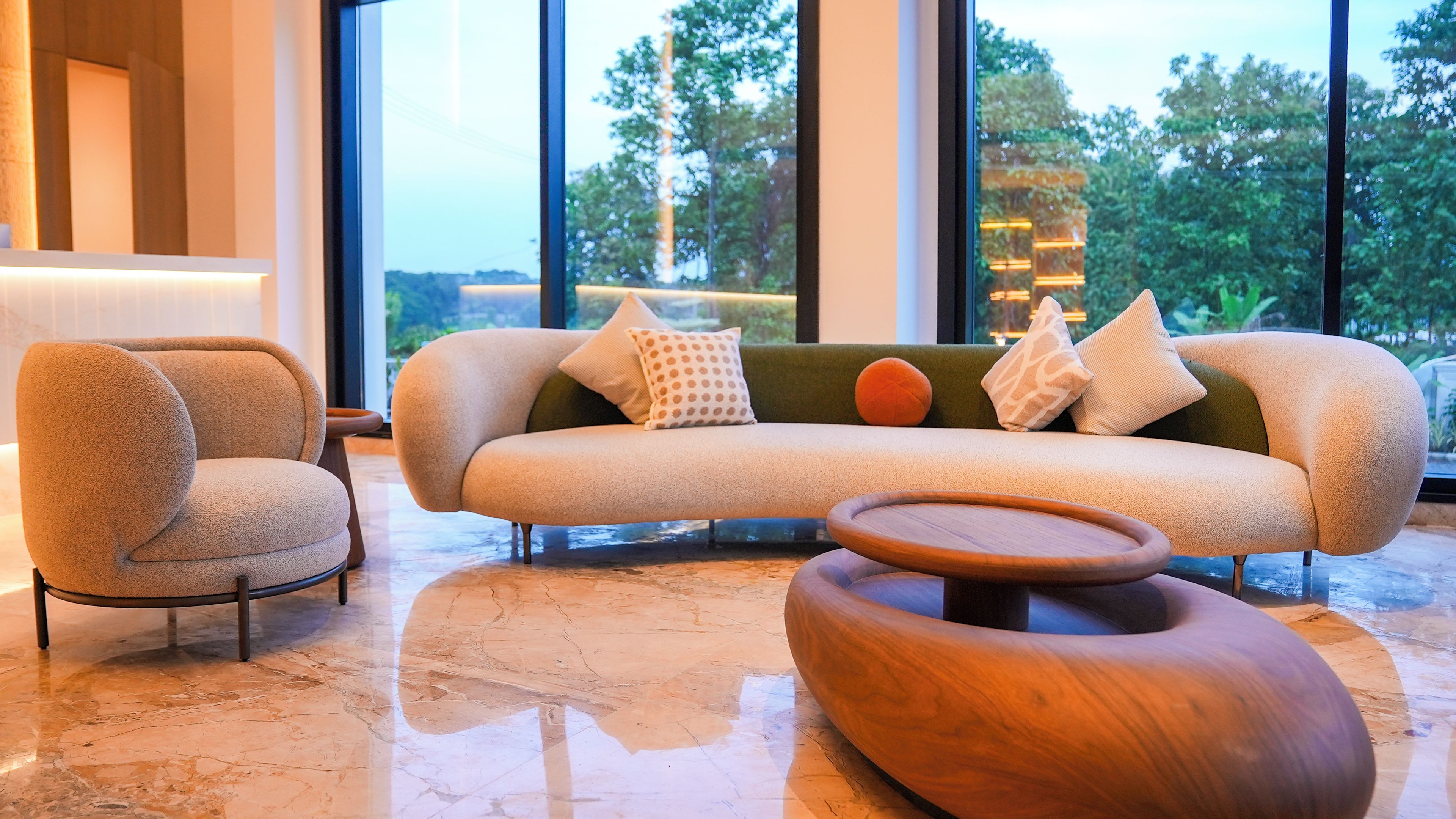 A modern living room with a curved sofa, a round wooden coffee table, and a matching armchair.