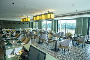 A restaurant with a high ceiling, large windows, and a variety of seating arrangements including tables and chairs. - Travancore Palace, Cochin (Aluva)