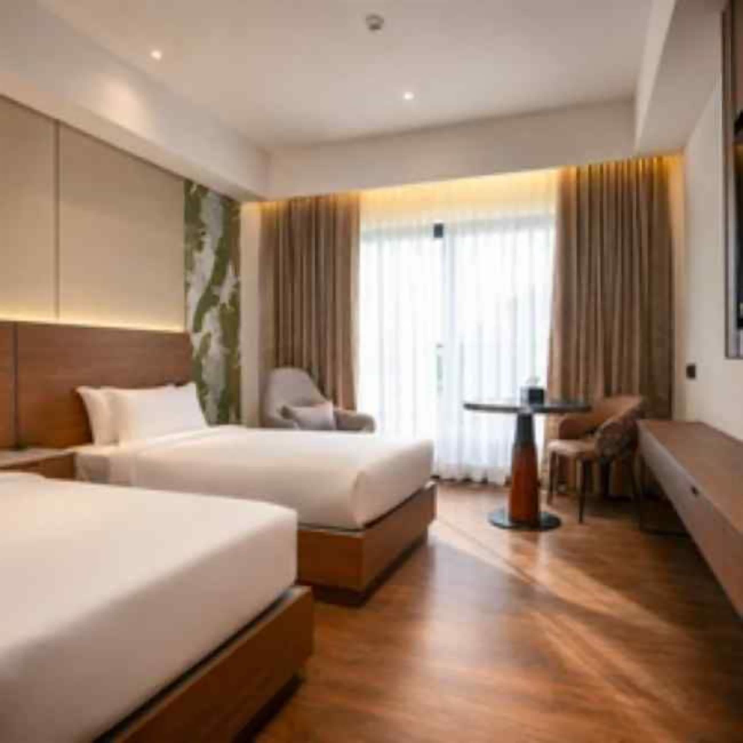 Ett hotellrum med två sängar, en sittgrupp och ett stort fönster med gardiner.