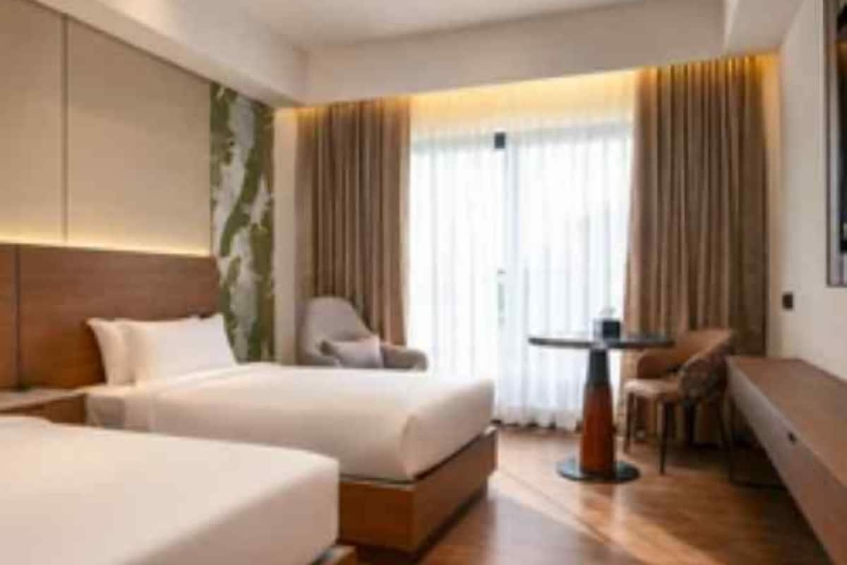 A hotel room with two beds, a seating area, and a large window with curtains.