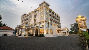 A grand hotel with a prominent entrance, multiple floors, and a sign indicating amenities like a banquet hall, deluxe rooms, and a restaurant. - Travancore Palace, Cochin (Aluva)