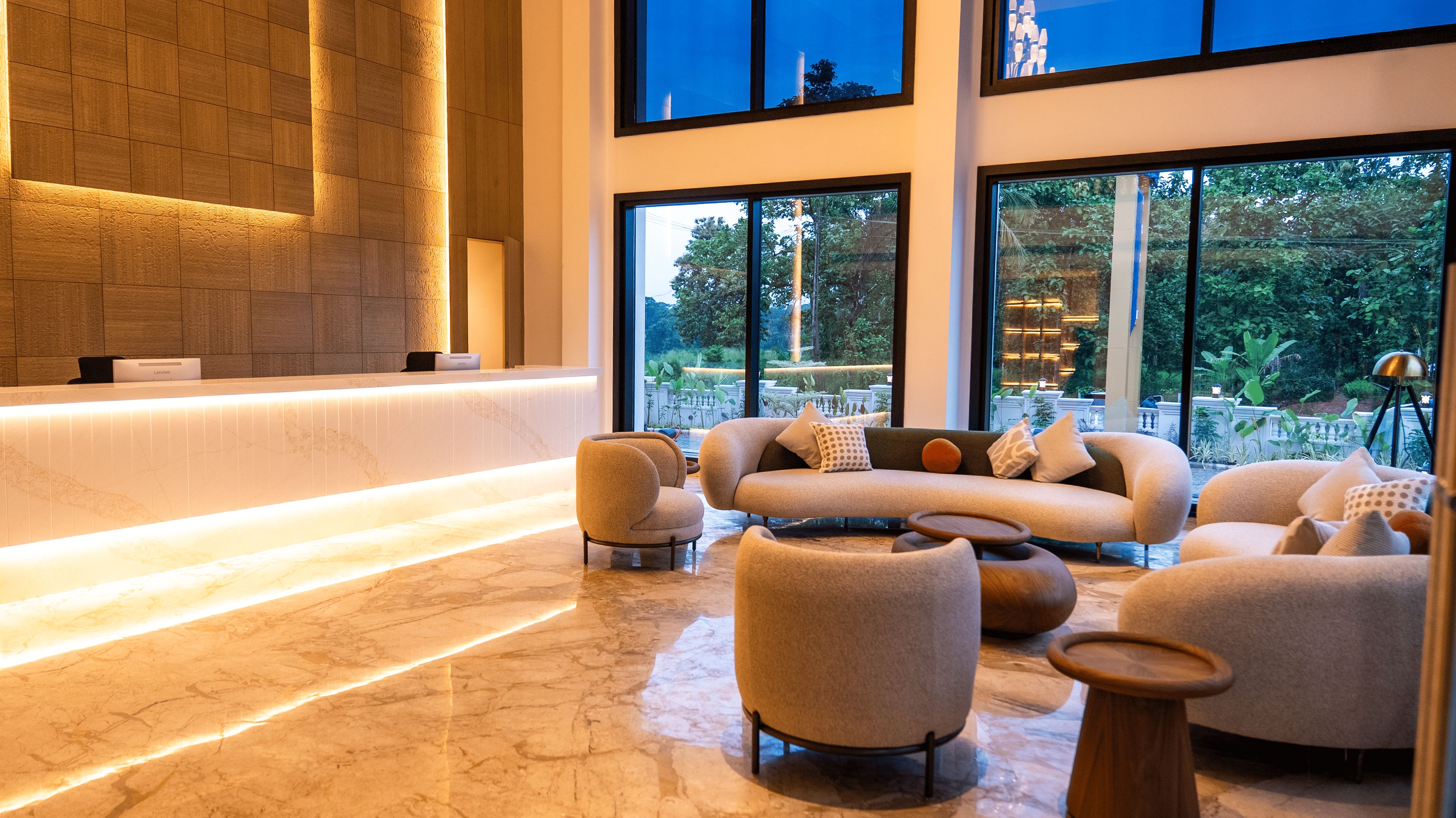 A modern lobby with a reception desk, seating area, and large windows offering a view of the outdoors.