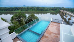 A rooftop infinity pool with a glass edge, overlooking a calm lake and lush greenery. - Travancore Palace, Cochin (Aluva)