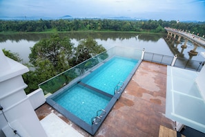 A rooftop infinity pool with a glass edge, overlooking a calm lake and lush greenery. - Travancore Palace, Cochin (Aluva)