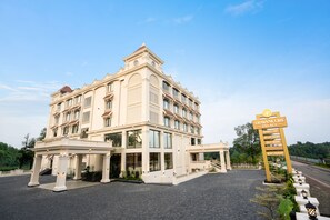 A large, multi-story hotel with a grand entrance, a sign indicating amenities like a banquet hall and restaurant, and a paved driveway leading to the entrance. - Travancore Palace, Cochin (Aluva)