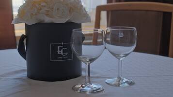 A table with a black mug and two wine glasses, a bouquet of white flowers, and a window with curtains.
