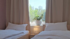 Une chambre avec deux lits, une fenêtre avec des rideaux, une table de chevet avec une lampe et une plante en pot.