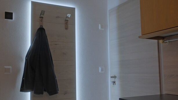 Une pièce avec une porte en bois, un manteau accroché à un crochet et un comptoir noir.