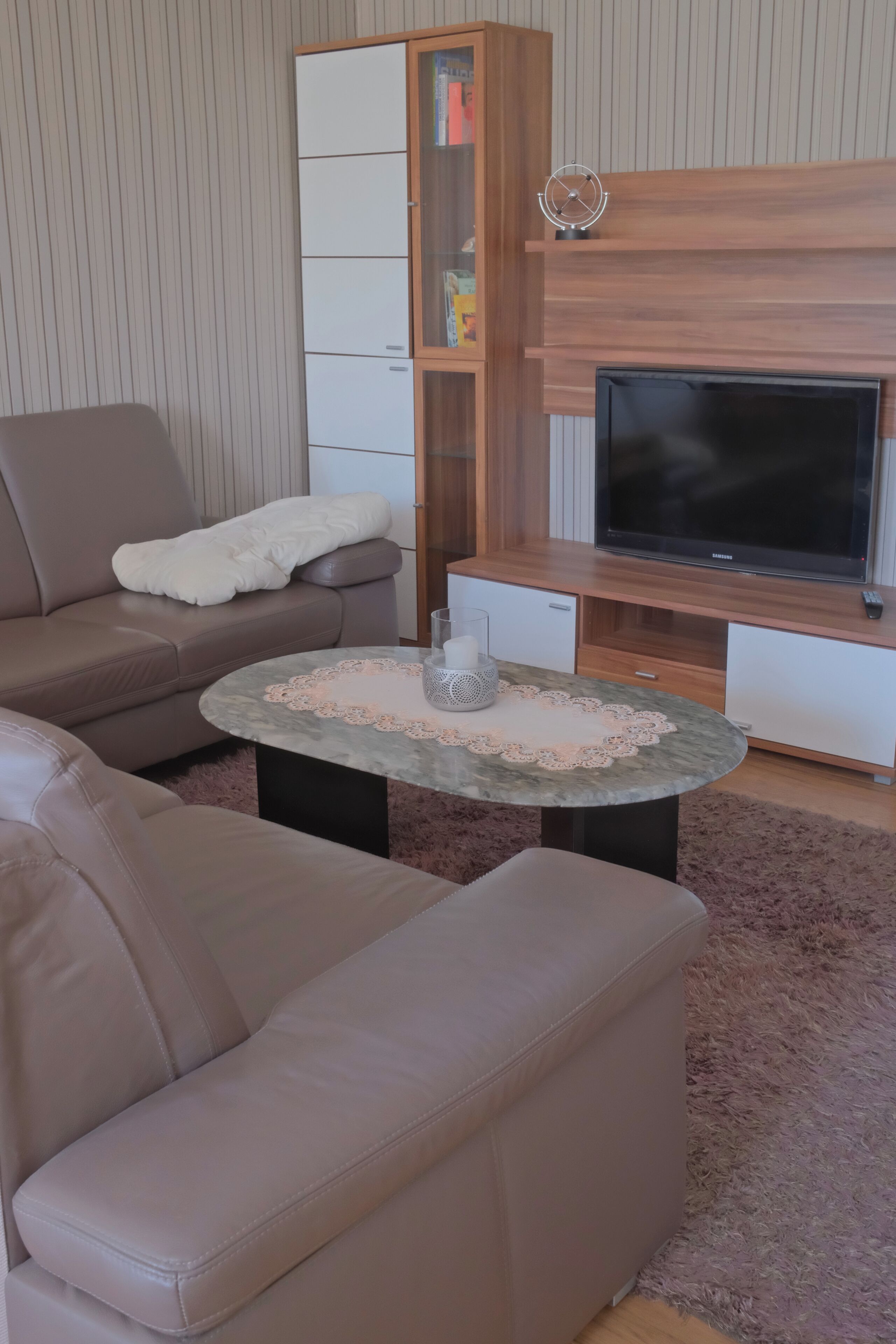A living room with a sofa, a coffee table with a decorative doily, a television, and a wooden cabinet.