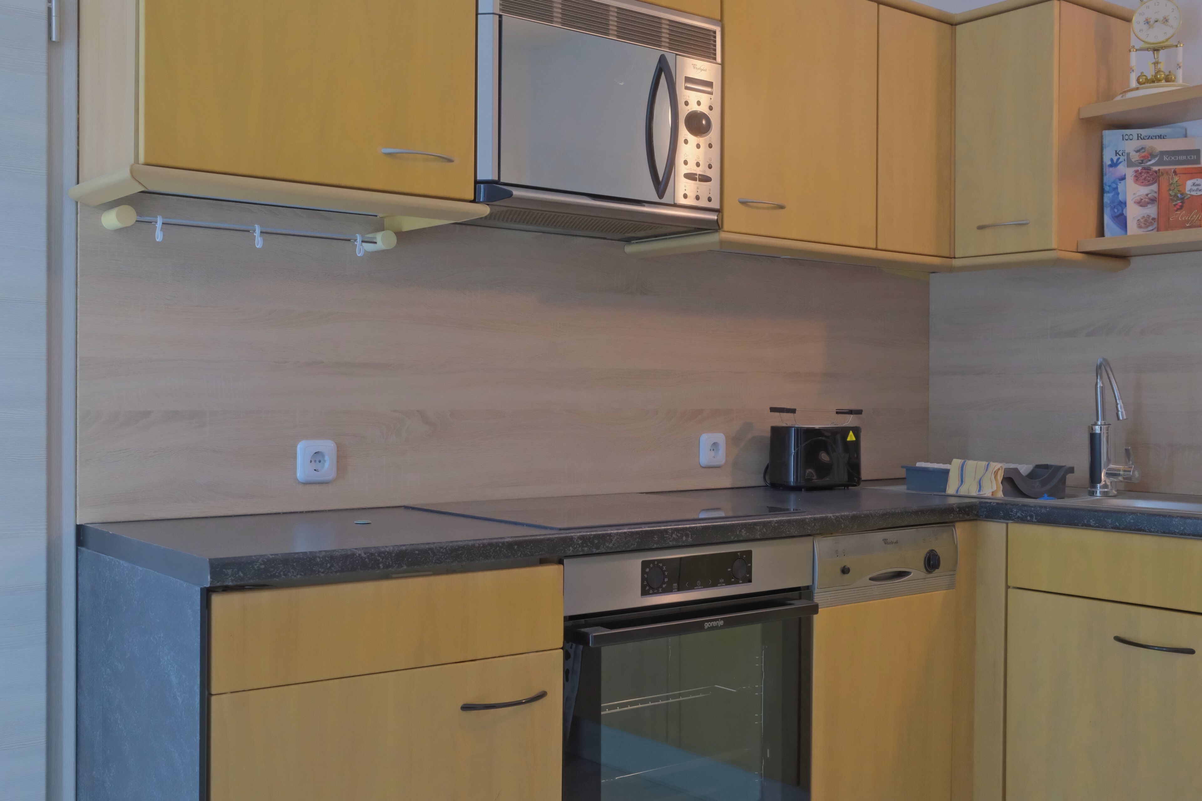 Een keuken met houten kastjes, een magnetron, een broodrooster en een spoelbak.