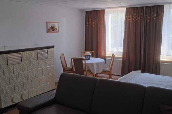 Une chambre d’hôtel comprenant un lit, un canapé, une table à manger avec des chaises, un petit coin cuisine et une fenêtre avec des rideaux.