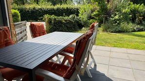 Une terrasse extérieure avec une table et des chaises, entourée d’un jardin.