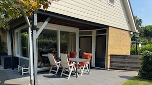 A covered patio with a table and chairs, a brick wall, and a glass door leading to a garden.