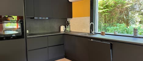 Una cucina moderna con mobili scuri, forno integrato, macchina da caffè e una finestra con vista sul verde.