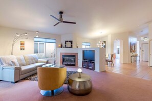 A modern living room with a sofa, a coffee table, a fireplace, a television, and a ceiling fan. - Casa Christie | Charming 2BR | Firepit | Dog Friendly (Tucson)