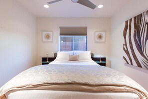 Ein Schlafzimmer mit einem Bett, einem Deckenventilator, einem Fenster mit Jalousien und zwei Nachttischen mit Lampen.