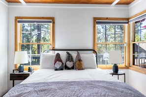 Un dormitorio con una cama, dos mesitas de noche, una lámpara y tres almohadones decorativos con forma de gnomos.