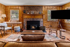 Ein gemütliches Wohnzimmer mit Kamin, Holzwänden, einer Couch, einem Couchtisch und einem Fernseher.
