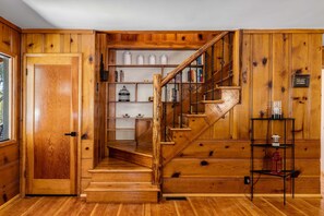A wooden staircase leading to a book-filled room with a wooden door and a shelf with various items. - Lundquist House | Luxury 4BR | Wraparound Deck & Hot Tub | Antler Chandelier | Idyllwild (Idyllwild)