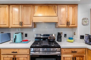 A kitchen with wooden cabinets, a stove, a kettle, and various kitchen appliances. - Lundquist House | Luxury 4BR | Wraparound Deck & Hot Tub | Antler Chandelier | Idyllwild (Idyllwild)