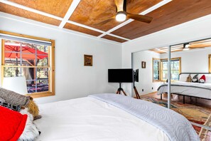 Ein Schlafzimmer mit einem Bett, einem Fernseher auf einem Schrank, einem Deckenventilator und einem großen Fenster mit Blick auf einen Regenschirm.