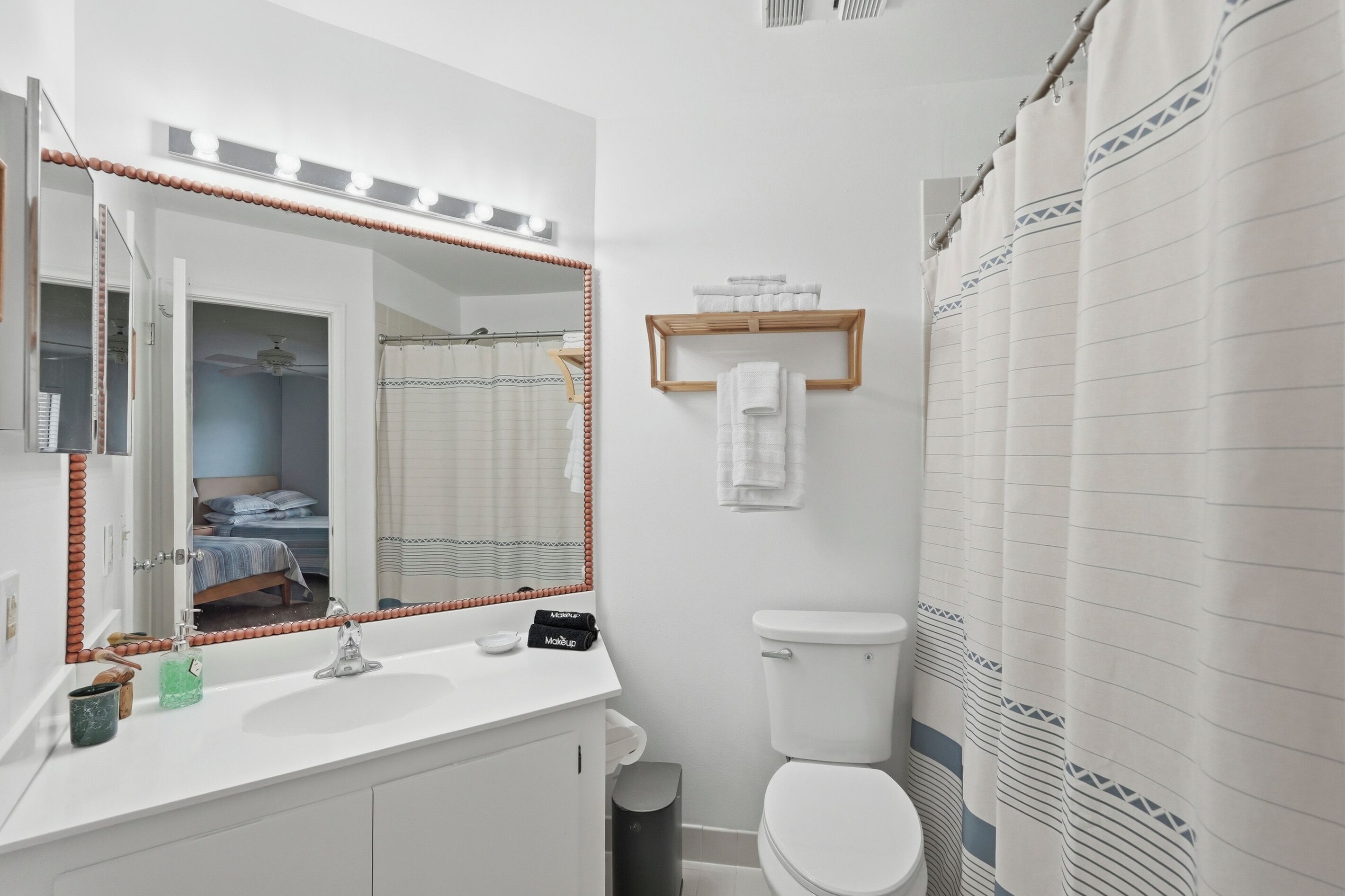 A bathroom with a white sink, mirror, and toilet. There is a towel rack with folded towels and a shower curtain with a geometric pattern.