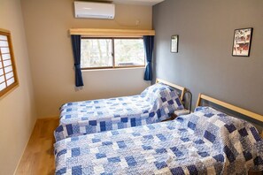 Quarto com duas camas, janela com cortinas, ar-condicionado fixado na parede e um quadro emoldurado.