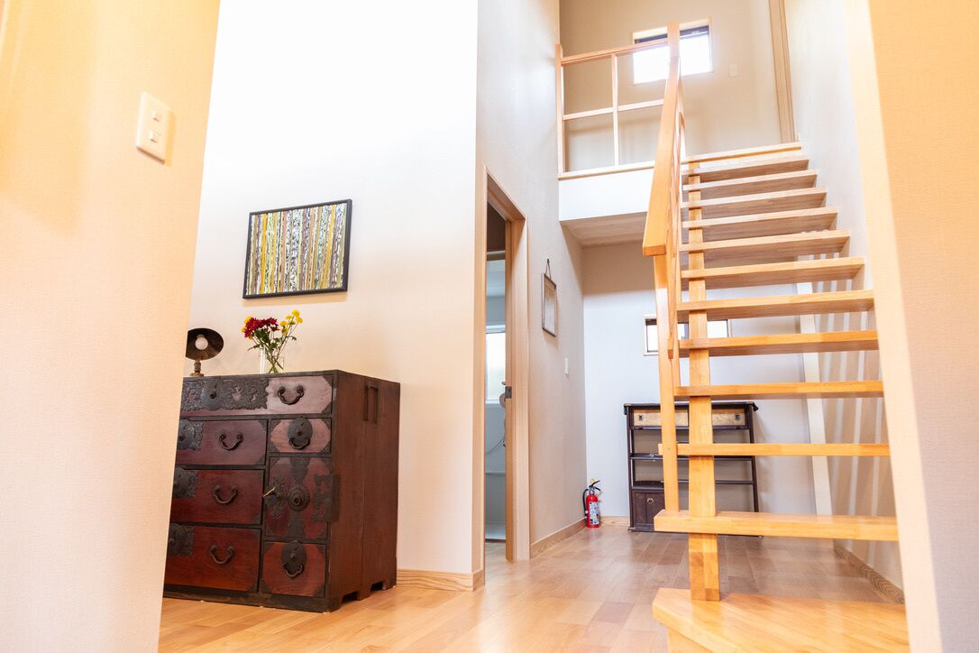 A staircase leading to an upper level, a wooden cabinet with drawers, and a framed artwork on the wall.
