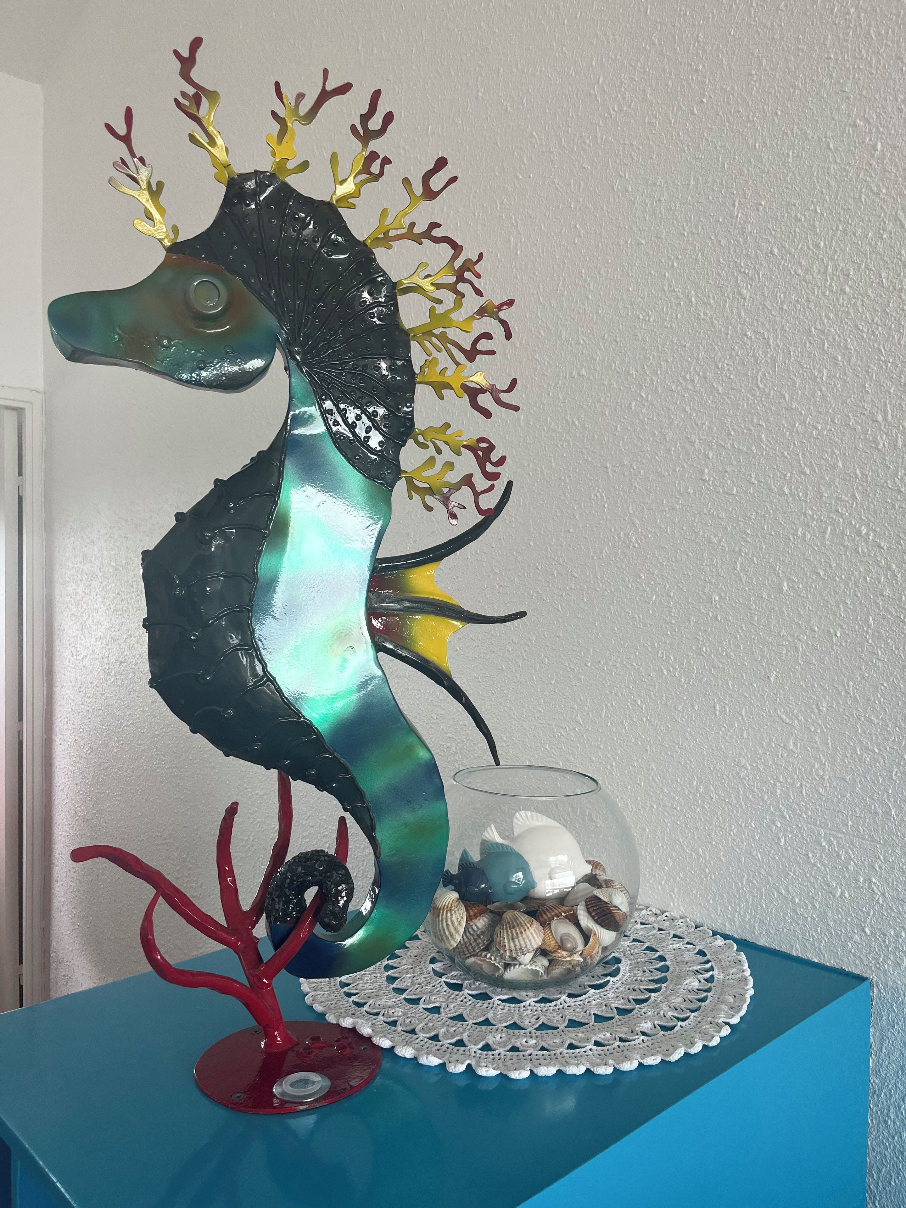 A decorative seahorse sculpture on a blue table with a glass bowl of seashells.