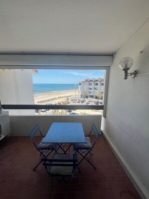 Ein Balkon mit Tisch und Stühlen mit Blick auf Strand und Gebäude.