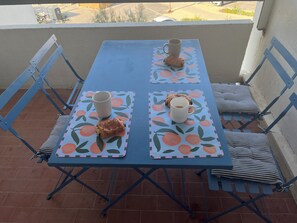 A blue metal table with two chairs, each with a cushion. The table has two placemats with a fruit pattern. - Hippo Duplex with parking, right on the water's edge in Carnon (Mauguio)